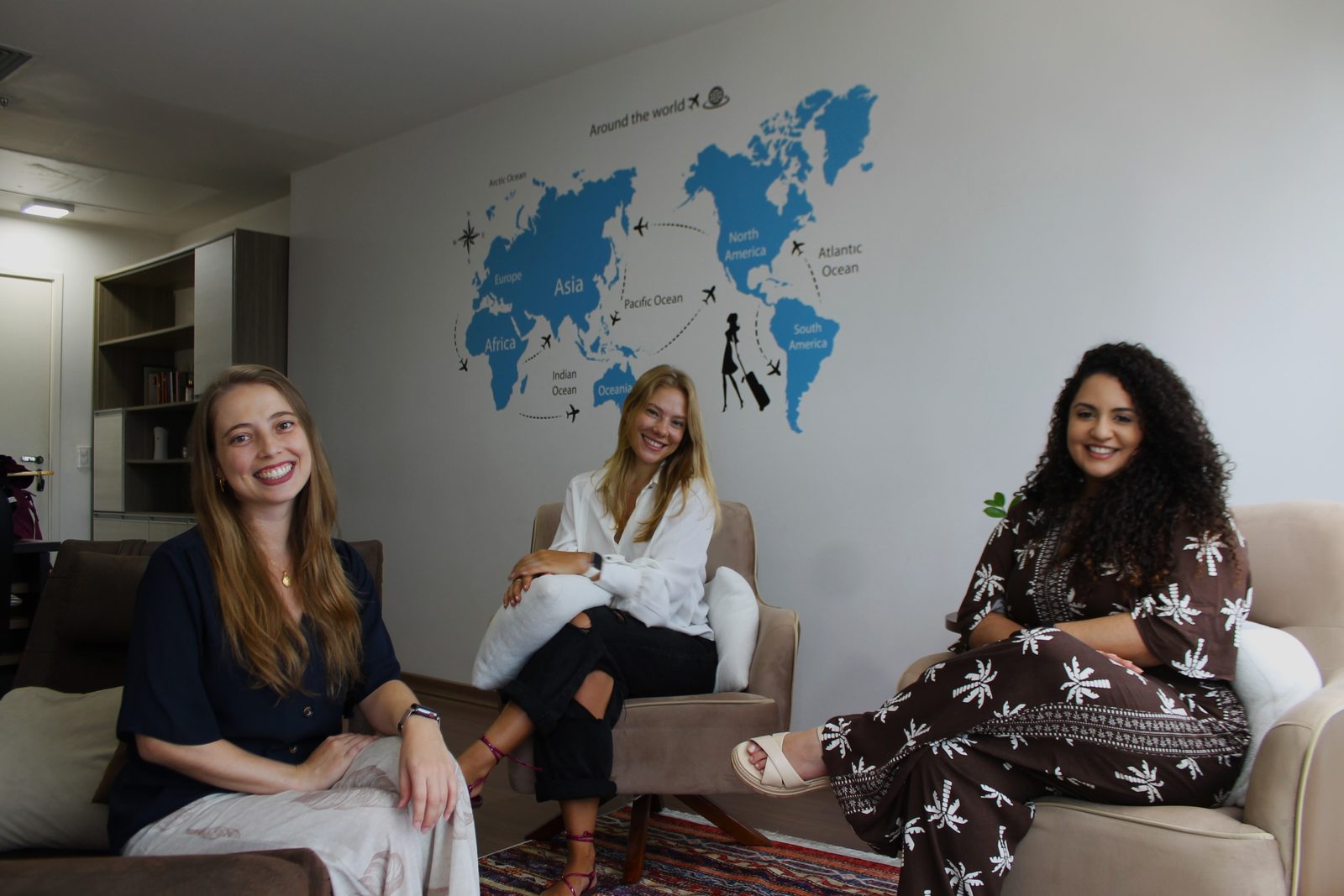 Profissionais da Serenitah sorrindo, sentadas em poltronas numa sala com mapa-múndi na parede